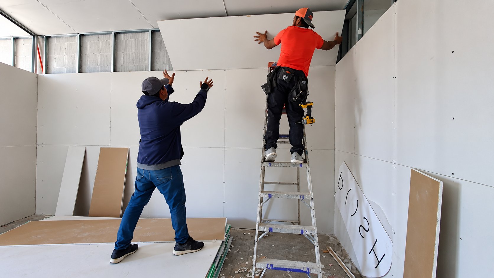 Dos instaladores colocan placas de tablaroca en los muros del consultorio