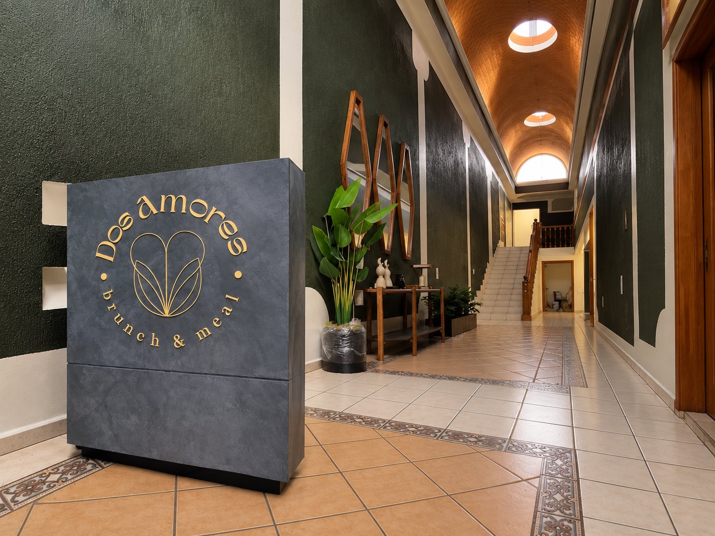 Mueble de recepción con acabado gris y logotipo dorado de Dos Amores, frente a un pasillo de muros verdes y bóveda de ladrillo