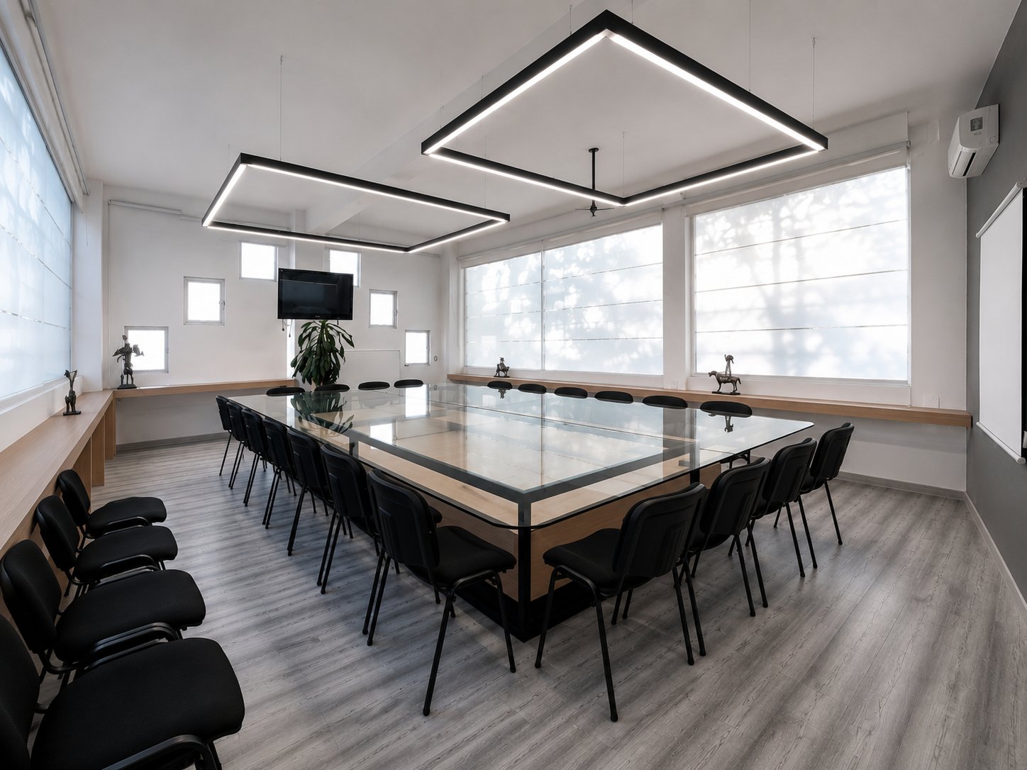 Sala de juntas con mesa de vidrio sobre base de madera y herrería, sillas negras, repisa perimetral de madera y lámparas lineales cuadradas