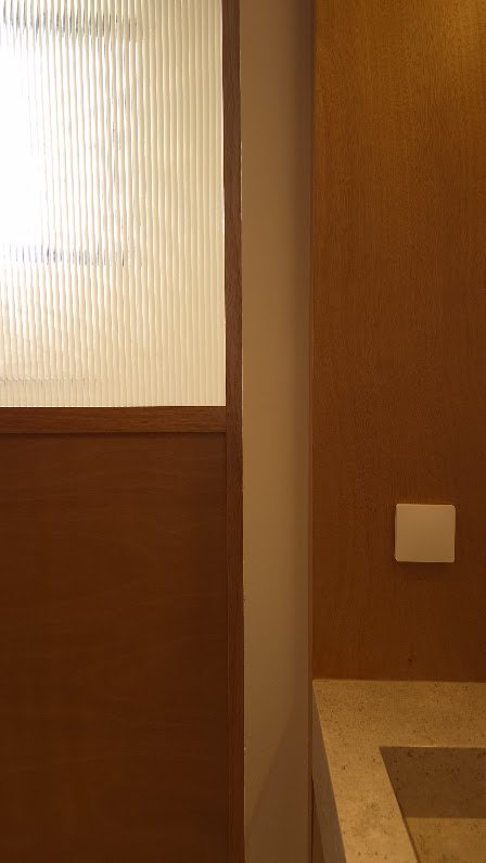 Detalle del cancel de vidrio acanalado junto al muro de madera y la cubierta de piedra