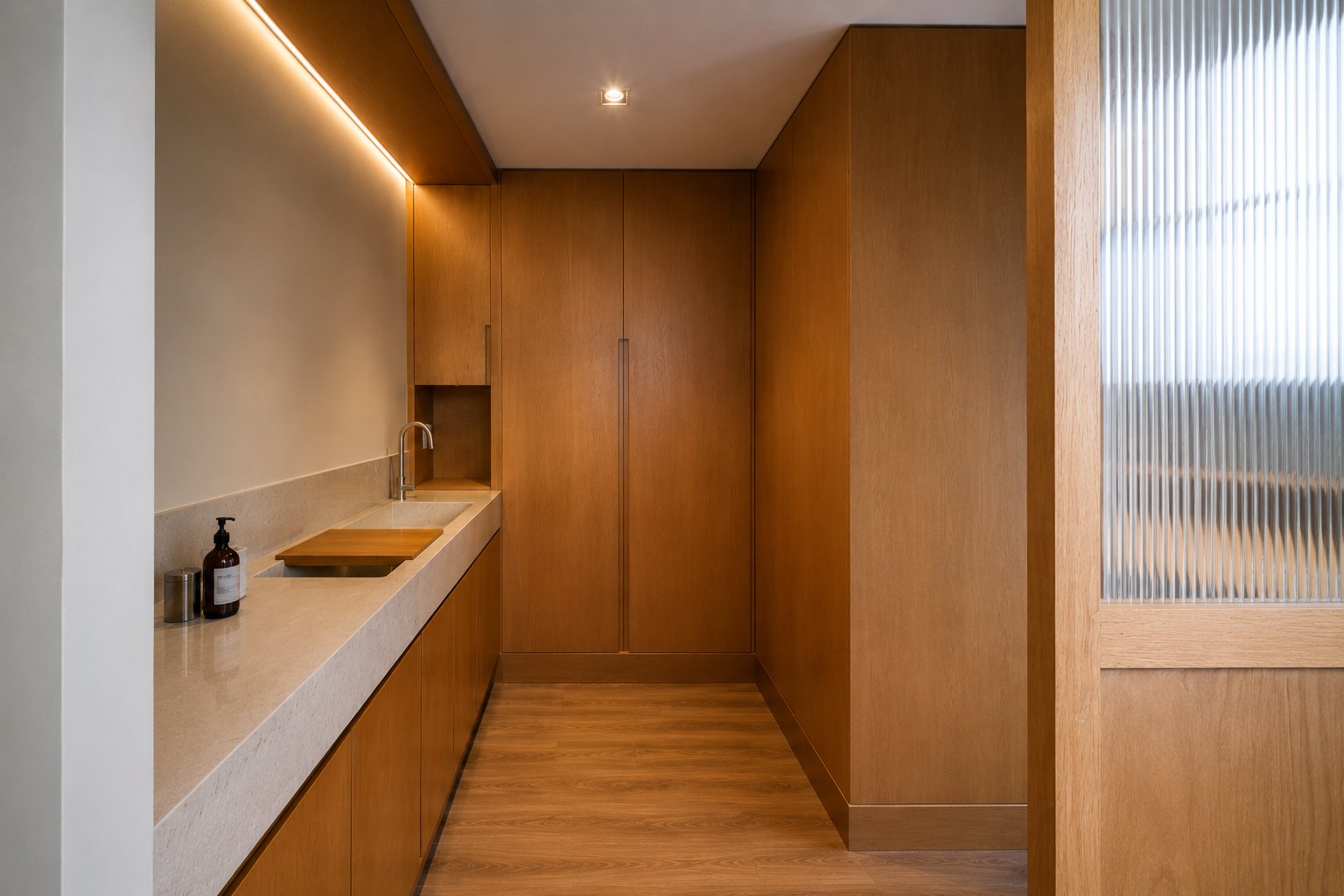 Vista del vestidor: cubierta de piedra con gabinetes bajos, clóset de madera al fondo y cancel de vidrio acanalado